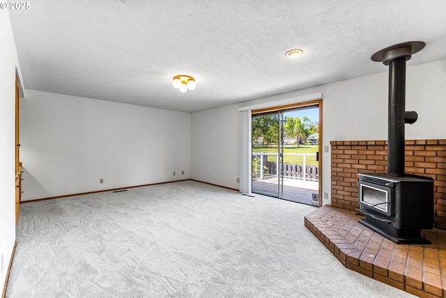 unfurnished living room featuring carpet floors, a wood stove, visible vents, baseboards, and a textured ceiling