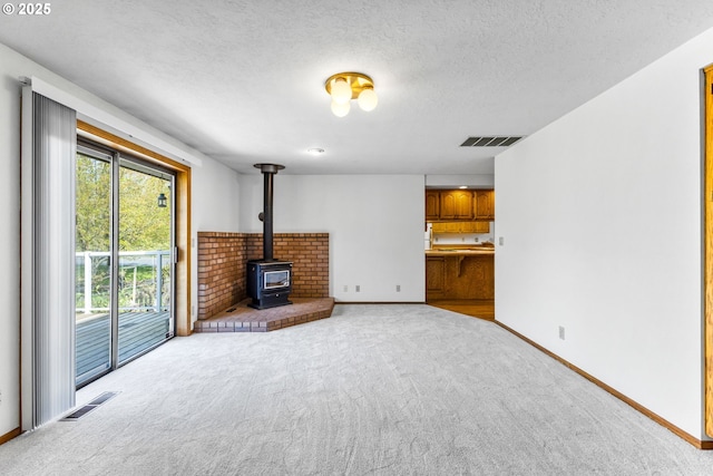 unfurnished living room featuring baseboards, light carpet, a wood stove, and visible vents