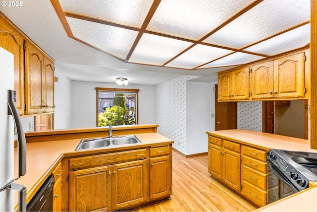 kitchen with a peninsula, light wood-style floors, wallpapered walls, a sink, and black appliances
