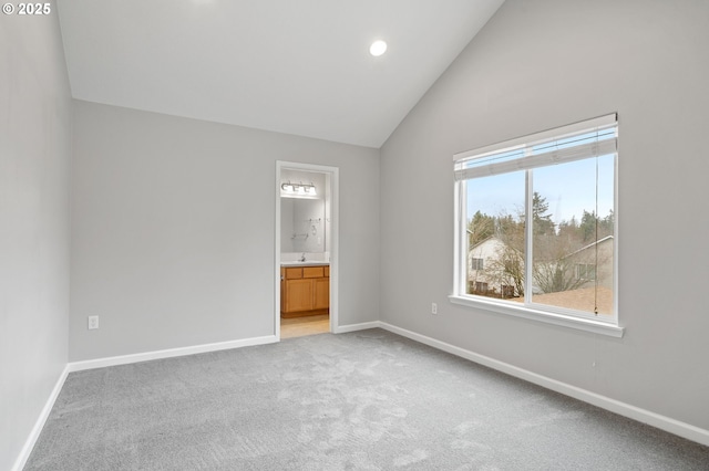 unfurnished bedroom featuring high vaulted ceiling, ensuite bathroom, a sink, baseboards, and light colored carpet