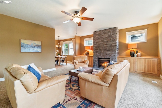 living room with a stone fireplace, light colored carpet, baseboards, and ceiling fan with notable chandelier