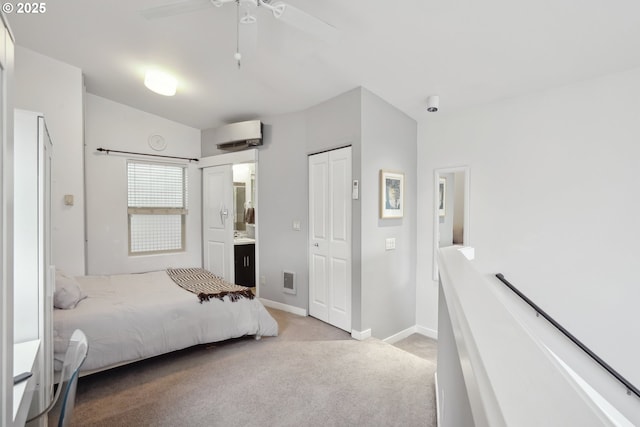 carpeted bedroom with baseboards, ensuite bathroom, a wall unit AC, a closet, and a ceiling fan