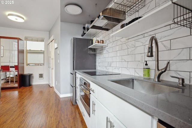 kitchen featuring a sink, oven, open shelves, tasteful backsplash, and white cabinetry