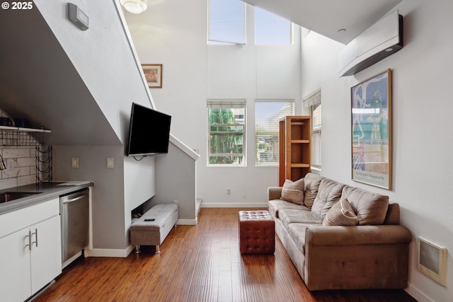 living area with wood finished floors, a wall mounted AC, baseboards, and a high ceiling