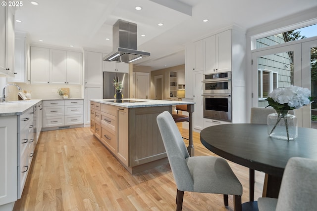 3505 SW Beaverton Ave, Portland, OR 97239 - kitchen featuring island range hood, appliances with stainless steel finishes, light wood-style flooring, an island with sink, and white cabinetry