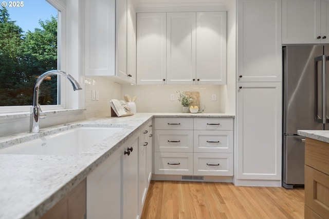 3505 SW Beaverton Ave, Portland, OR 97239 - kitchen featuring freestanding refrigerator, white cabinets, light wood-style flooring, tasteful backsplash, and light stone counters