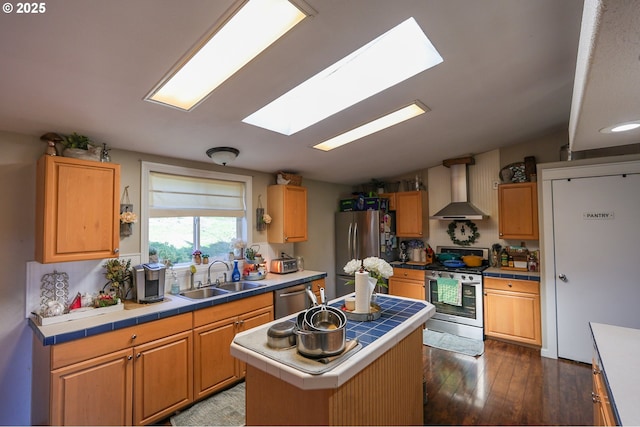 kitchen featuring a sink, wall chimney range hood, appliances with stainless steel finishes, tile counters, and dark wood-style floors