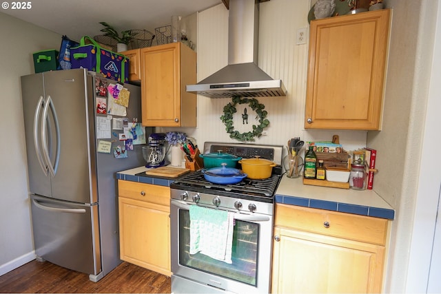 kitchen featuring tile counters, wall chimney range hood, dark wood-type flooring, and appliances with stainless steel finishes