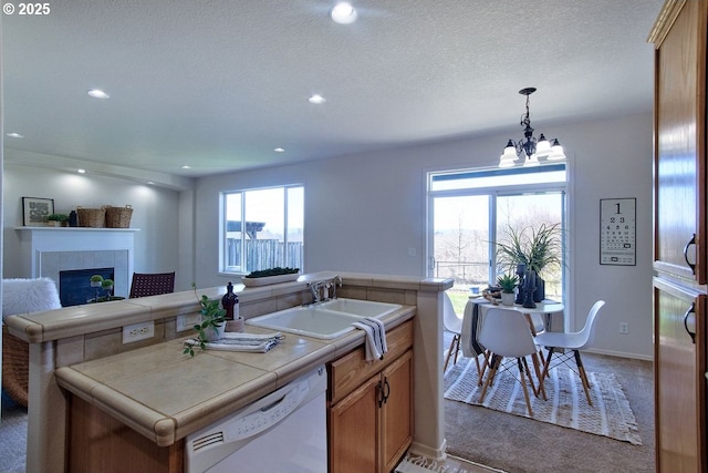 kitchen featuring tile countertops, a fireplace, a sink, dishwasher, and a chandelier