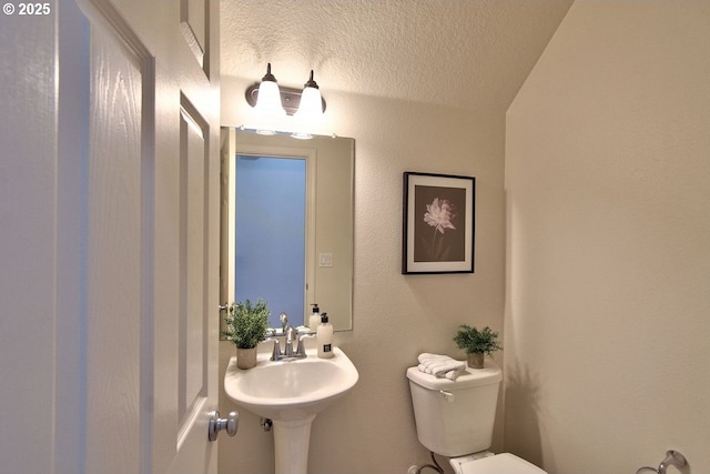 half bathroom featuring a sink, toilet, and a textured ceiling