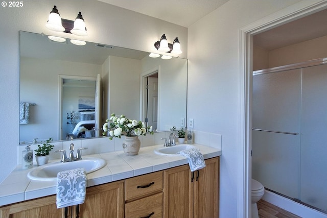 full bathroom featuring double vanity, toilet, a stall shower, and a sink