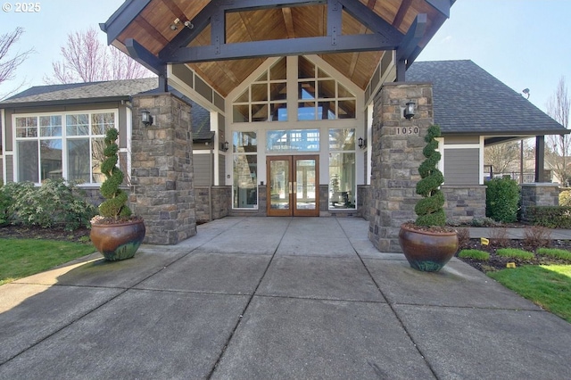 entrance to property with french doors, stone siding, and roof with shingles