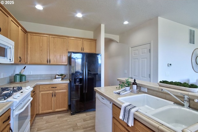 kitchen featuring white appliances, visible vents, arched walkways, a sink, and light wood-type flooring