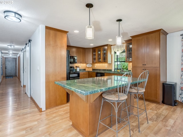 kitchen featuring brown cabinets, light wood-style flooring, a kitchen breakfast bar, and black appliances