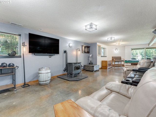 living area featuring a wood stove, a textured ceiling, finished concrete floors, and visible vents