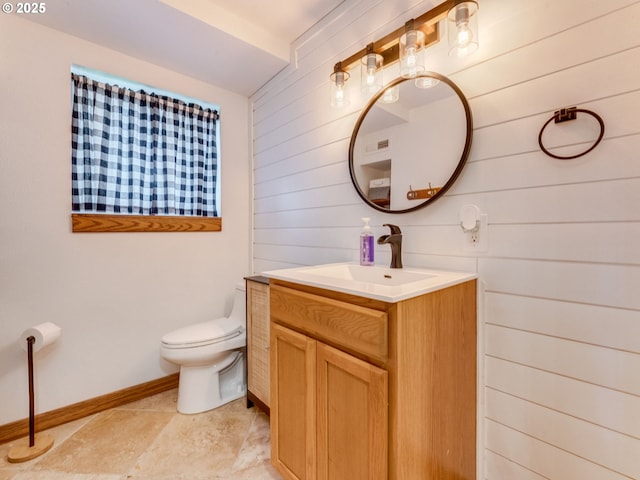 bathroom featuring toilet, wooden walls, vanity, and baseboards
