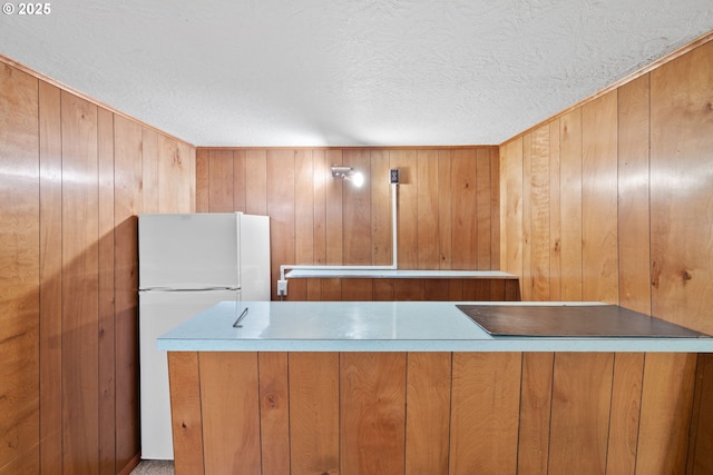 1627 NE 143rd Ave, Portland, OR 97230 - kitchen with freestanding refrigerator, a textured ceiling, wood walls, and brown cabinetry