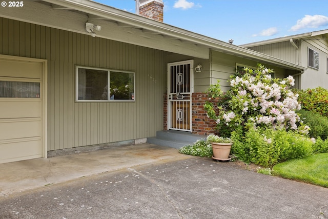 1627 NE 143rd Ave, Portland, OR 97230 - view of exterior entry with a chimney, driveway, a garage, and brick siding