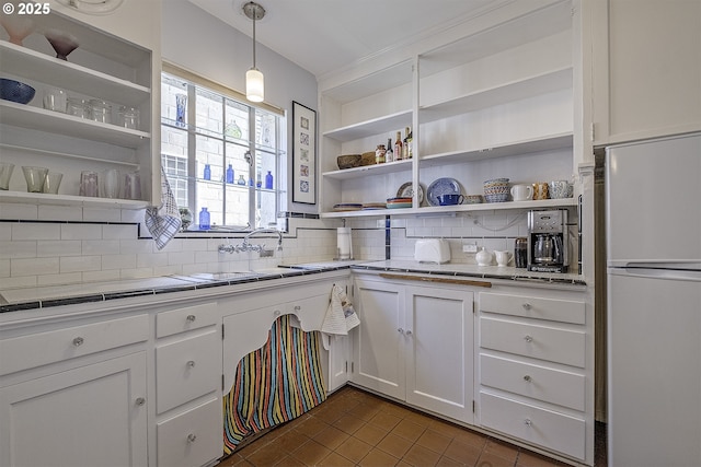 kitchen with freestanding refrigerator, open shelves, dark tile patterned floors, white cabinets, and tasteful backsplash