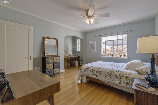 bedroom featuring crown molding, arched walkways, baseboards, and light wood-type flooring