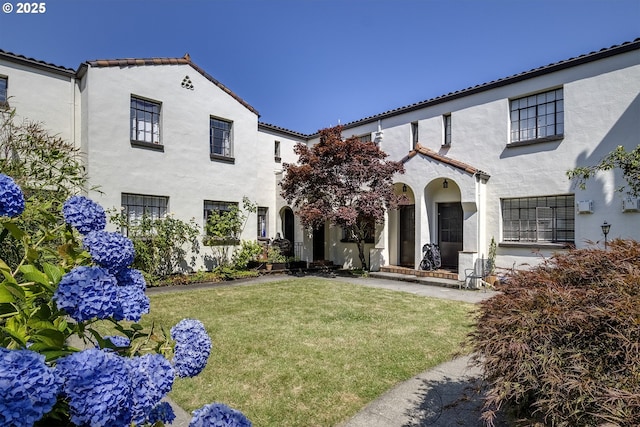 view of front of house with a front lawn, stucco siding, and a tile roof