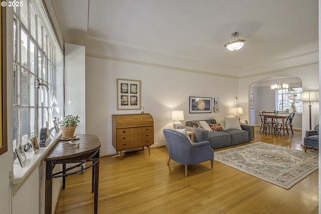 living area with arched walkways, baseboards, and light wood-type flooring