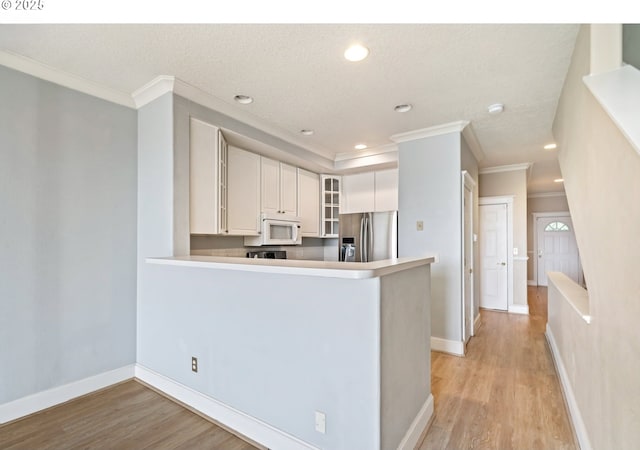 kitchen featuring white microwave, stainless steel fridge, ornamental molding, glass insert cabinets, and light wood-style floors