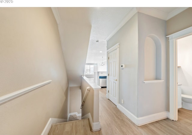 hall with an upstairs landing, light wood-style floors, baseboards, and ornamental molding