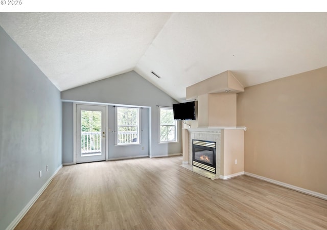 unfurnished living room featuring light wood-style floors, healthy amount of natural light, a fireplace, vaulted ceiling, and baseboards