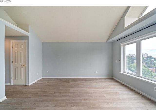 unfurnished room featuring vaulted ceiling, light wood-style flooring, and baseboards