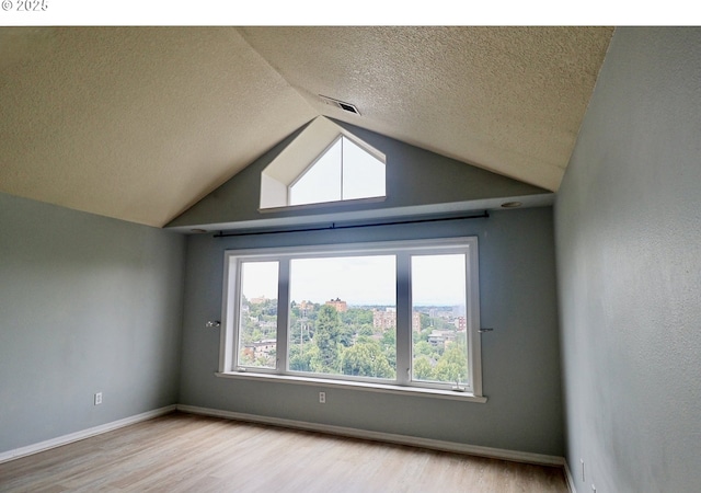 empty room featuring wood finished floors, a textured ceiling, lofted ceiling, and baseboards