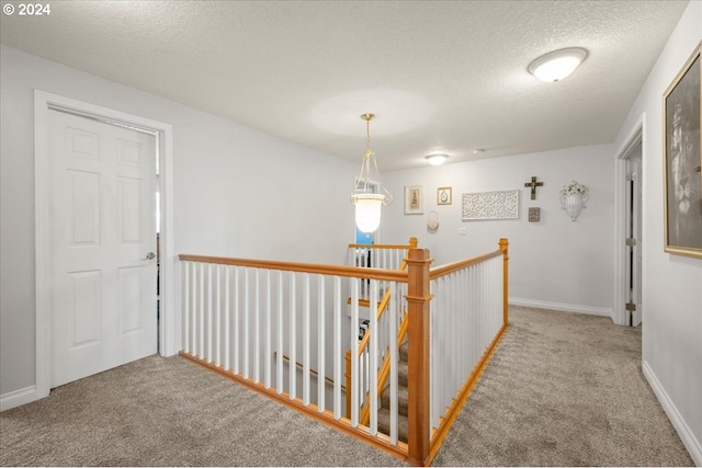 hallway with baseboards, carpet flooring, a textured ceiling, and an upstairs landing
