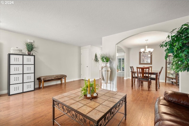 living area featuring arched walkways, a textured ceiling, a notable chandelier, and wood finished floors