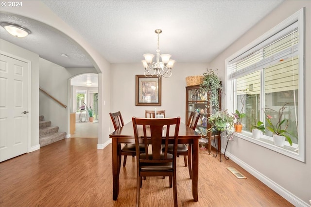 dining area with visible vents, arched walkways, light wood-type flooring, baseboards, and stairs