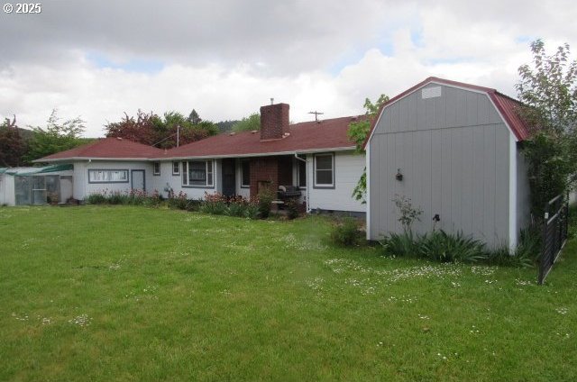 back of house featuring a chimney, a yard, an outbuilding, and a gambrel roof