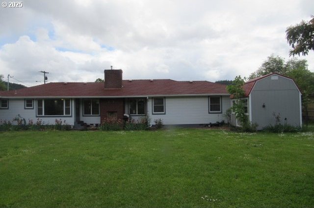 rear view of property featuring a chimney, a yard, an outdoor structure, and a shed