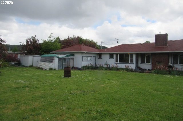 back of house featuring a shed, a chimney, a yard, and an outdoor structure