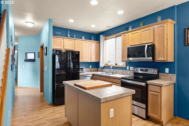 kitchen with light brown cabinetry, sink, light hardwood / wood-style flooring, a kitchen island, and stainless steel appliances