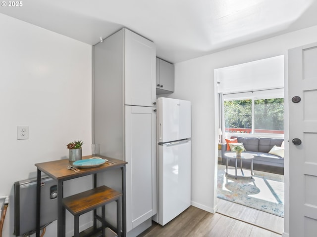 kitchen featuring baseboards, wood finished floors, freestanding refrigerator, and white cabinetry