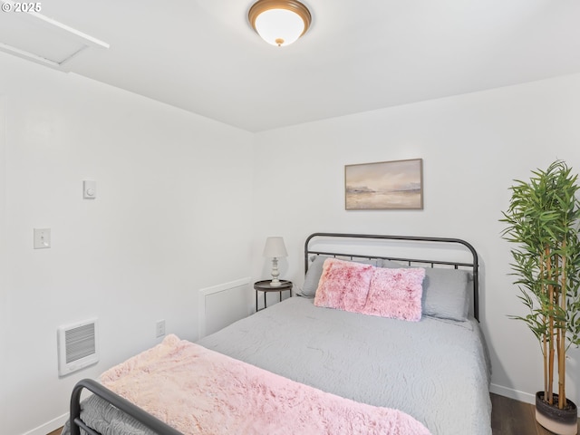 bedroom featuring heating unit, wood finished floors, attic access, and baseboards