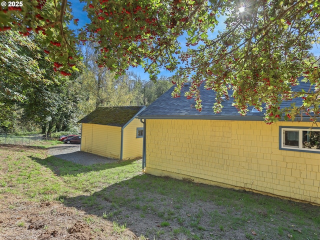 view of property exterior with a storage unit, an outbuilding, a lawn, and roof with shingles