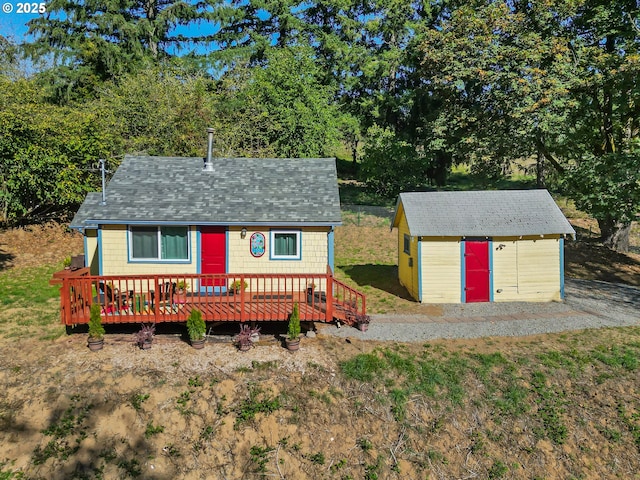 view of front of home featuring a shed, a shingled roof, and an outbuilding