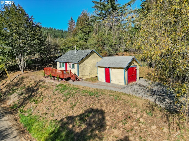 ranch-style house with a garage, a storage shed, a forest view, a wooden deck, and an outdoor structure