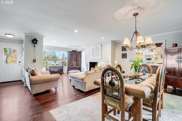 dining room featuring crown molding, wood finished floors, a chandelier, a brick fireplace, and recessed lighting