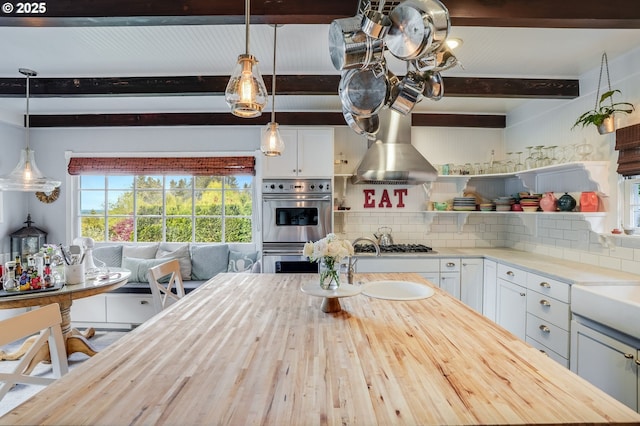 kitchen featuring beam ceiling, stainless steel appliances, decorative backsplash, wall chimney range hood, and white cabinets