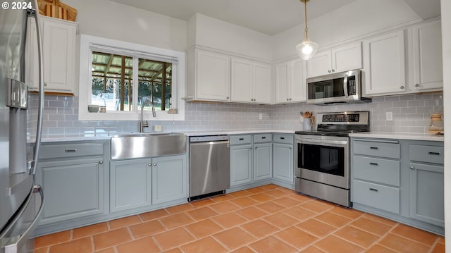 kitchen with stainless steel appliances, a sink, gray cabinetry, light countertops, and decorative backsplash