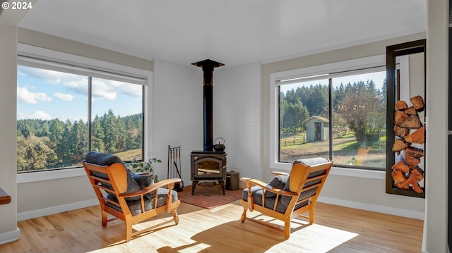sitting room with a wood stove, light wood-type flooring, and baseboards