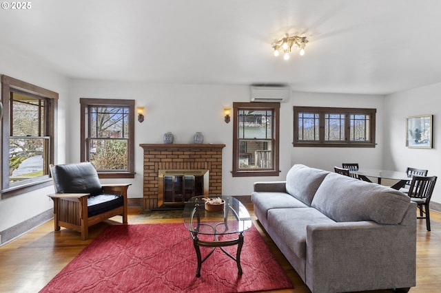 living room with an AC wall unit, a fireplace, wood finished floors, and baseboards