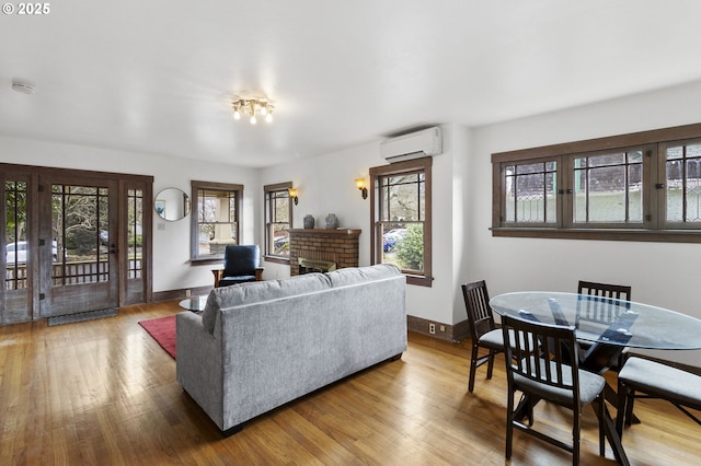 living room with a wall unit AC, a fireplace, baseboards, and wood finished floors