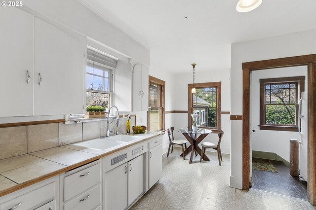 kitchen featuring pendant lighting, tile countertops, light floors, white cabinetry, and a sink